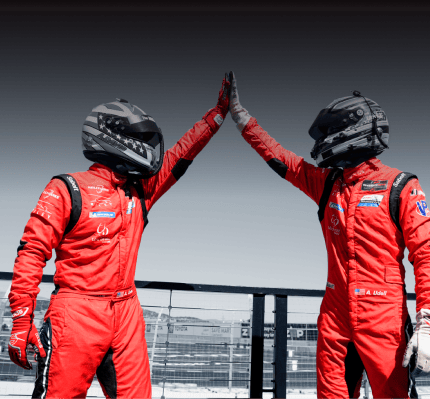 Two race car drivers in red suits high-fiving at the track.